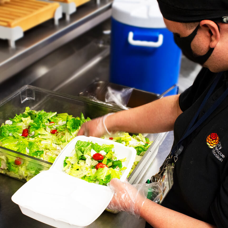 A city rescue mission volunteer prepares a leafy green and red tomato salad