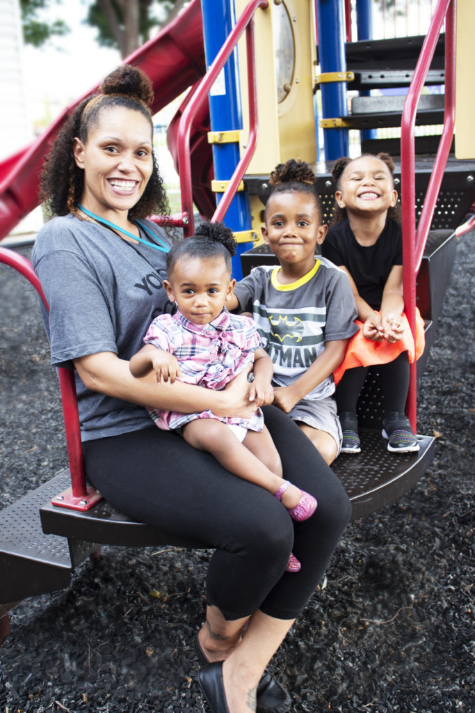 A young mother with her three young daughters pose on a playground smiling