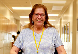 Our client Tracy smiles at the camera wearing red-framed glasses and yellow lanyard