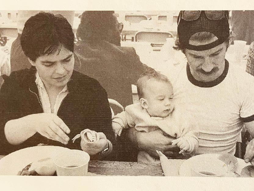 a black and white photo of a man, woman and their baby seated eating breakfast