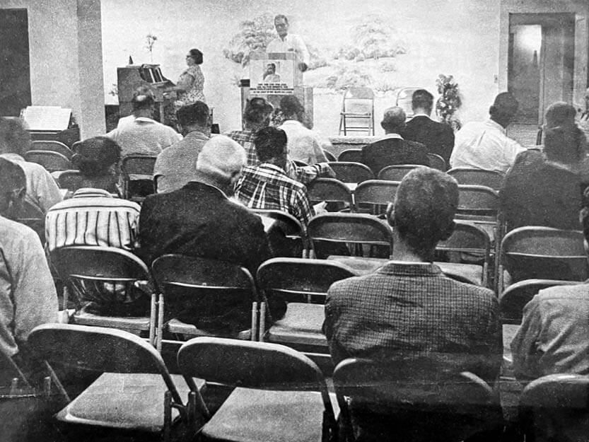 A black and white photo with multiple people seated listening to a sermon