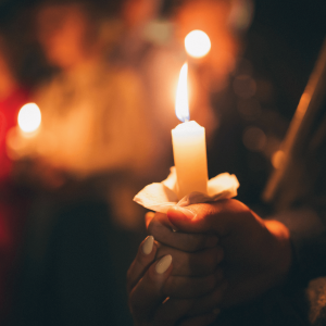 A hand holds a burning candle at a candle light vigil